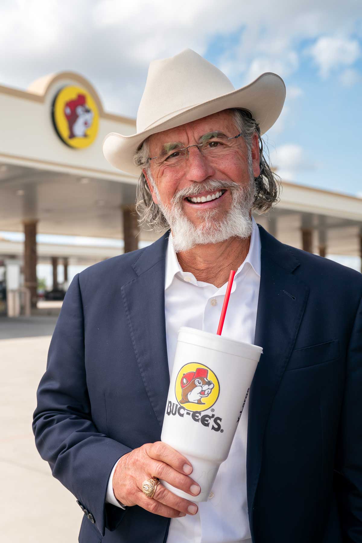 Former Student Arch Aplin poses in front of the iconic Buc-ee's gas station, holding a Buc-ee's cup and displaying his Aggie Ring with a smile.